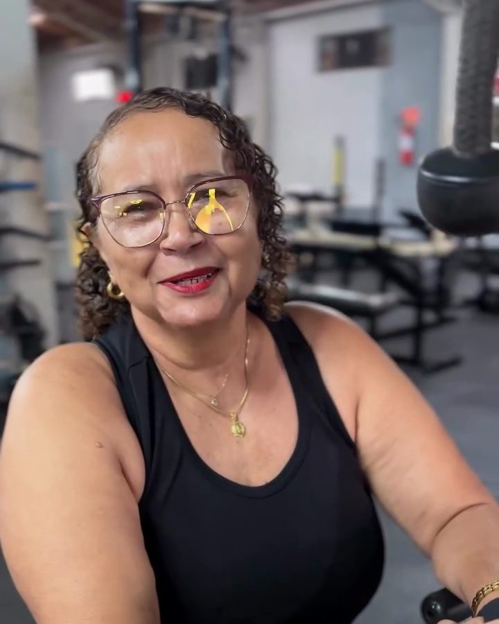 Dona Inês sorrindo, sentada num aparelho da academia.